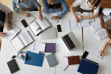 Above top view concentrated happy multiracial diverse team of young students using gadgets and books preparing for exams, working together on college project in library or campus, learning concept.