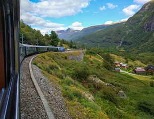 Flom, Norway - August 27, 2017: Beautiful view from the Flam railway train car to the high mountains and red wooden houses against the blue sky.