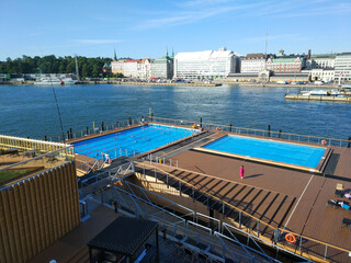 Plakat Helsinki, Finland - August 29, 2017: People bathe in an open public pool against the backdrop of the seaport and city buildings.