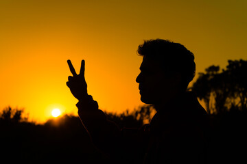 Young boy in silhouette at sunset on a beach of the Mediterranean Sea makes the symbol of peace with his fingers