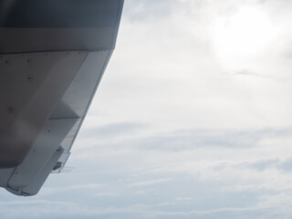 Obraz premium A fragment of the wing of a flying aircraft against the background of a cloudy sky and the sun peeking through the haze. View from the porthole. Soft focus