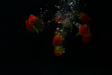 Strawberries falling into water with splash on black background
