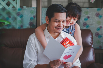 Asian little child daughters congratulating dad and giving him postcard and gift box with smiling...
