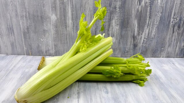Person puts a bunch of fresh celery on a gray wooden table