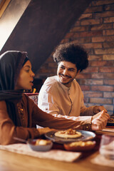 Young happy Muslim man enjoys in conversation with his wife meal at dining table.