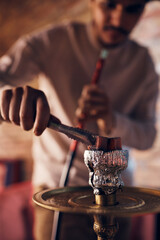 Close-up of Arabian man adds hot coal while smoking hookah.