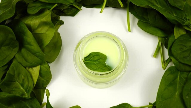 Jar with a skincare product based on spinach  is among a heap of the fresh spinach leaves