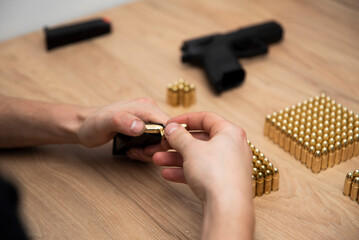 Mężczyzna wkładający naboje do magazynka swojej broni, w tle leży broń oraz naboje ułożone na stole