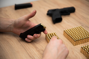 Mężczyzna trzymający naładowany magazynek od pistoletu, w tle leży broń oraz naboje na stole