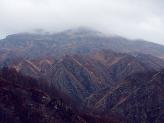 Rocky mountain ranges with dry yellow grass, bare autumn trees and overhanging clouds. Mountains of the North Caucasus