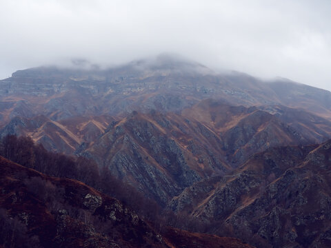 Rocky mountain ranges with dry yellow grass, bare autumn trees and overhanging clouds. Mountains of the North Caucasus