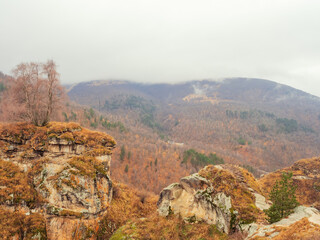 Rocky mountain ranges overgrown with dry grass and trees surrounded by mountainous woodland and thick white clouds. Autumn beauties of the Caucasus