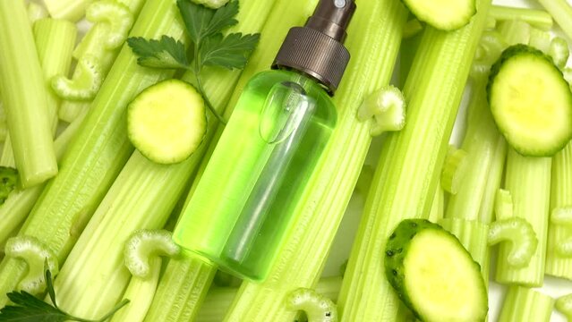 Bottle with cucumber and celery skincare product is on a heap of the fresh celery stalks and slices of the cucumber