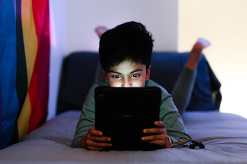 Ethnic boy using tablet on bed during bedtime at night