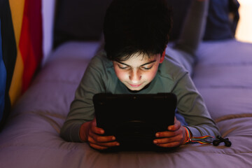 Ethnic boy using tablet on bed during bedtime at night