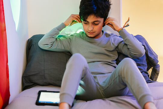 Ethnic teen boy putting on earbuds and using tablet