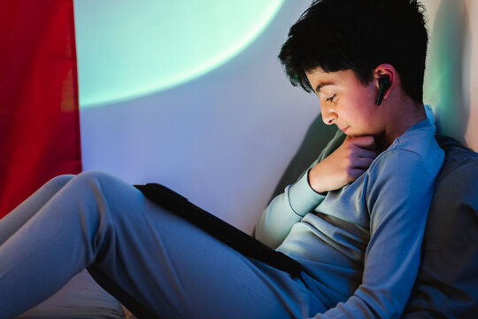 Ethnic teen boy on earbuds and using tablet