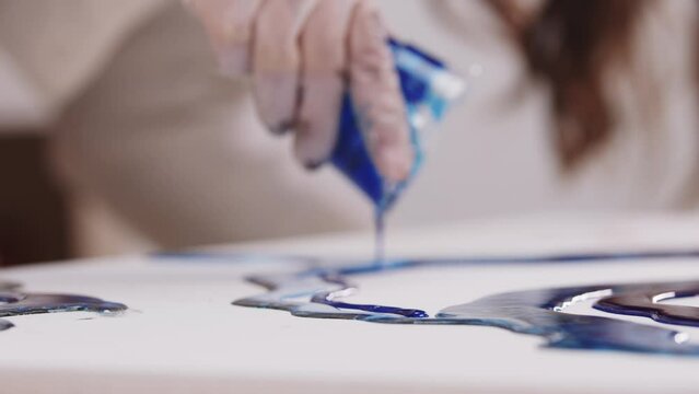 Artist pours deep blue epoxy resin on canvas from a plastic cup