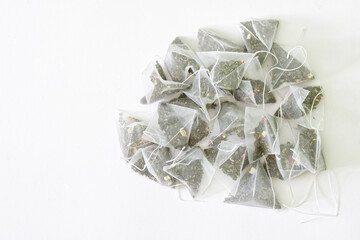 Bunch of tea bags-pyramids with green tea with the addition of fragrant fruits. Textured white background. Copy space for an inscription.