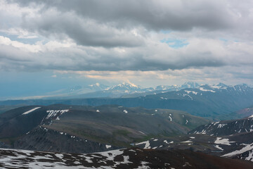 Dramatic aerial view to high snow mountain peak in sunlight in overcast. Atmospheric mountain landscape at high altitude with cloudiness. Awesome view to snowy mountain top in light under cloudy sky.