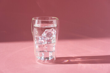 Glass of fresh pure cool water with ice cubes. Double walled glass. Hard light, deep shadow.