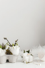 Easter egg shells with blooming snowdrops, bunny figurines, feathers, nest on aged white wooden table. Easter rustic still life. Simple stylish festive decoration on table. Happy Easter!