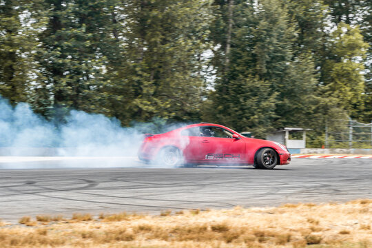Red Drift Car / Race car drifting around corner very fast with lots of smoke from burning tires on speedway / racetrack / drift track. Infiniti g35 v8. JDM car. Luxury red sport car.