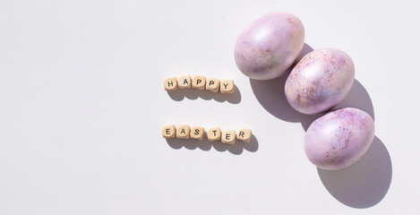 Easter concept banner. Purple eggs and wooden letters on a white background. Minimalism.