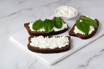 Slice of rye bread with cottage cheese and spinach on a wooden cutting board
