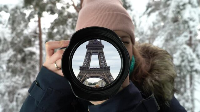 Young female photographer taking a picture in winter forest, but the lens reflecting Eiffel Tower in Paris. Dreams of travel and vacation
