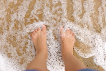 P&eacute;s femininos pisando na areia, molhados pela espuma da onda &agrave; beira do mar