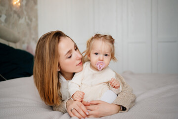 mom and baby daughter with baby nipple play and hug in bed. games with children.