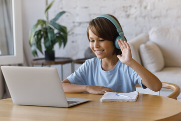 Happy little pre-teen boy in headphones smile look at laptop screen greeting tutor, start online...