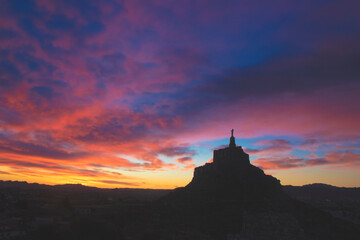 Silhouette of the medieval castle of Monteagudo, Murcia, Spain, with a cross on top. The sky shows the colors of dawn coloring the clouds above the sky