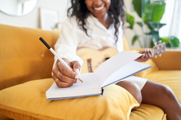 Close-up of a woman's hand writing in a notebook. New ideas inspirational singer composing music with a guitar at home.
