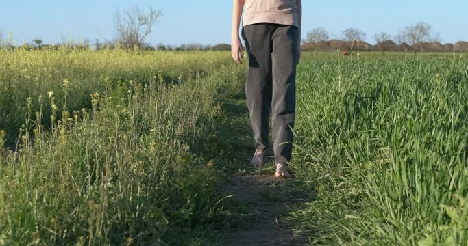 Walk with bare feet on the road. A girl stroll through a green summer meadow in the country.