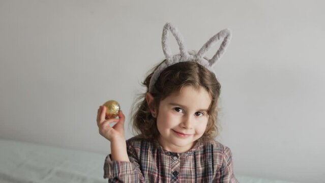 Portrait of funny caucasian girl with bunny ears with chocolate egg Easter symbol in spring month April March