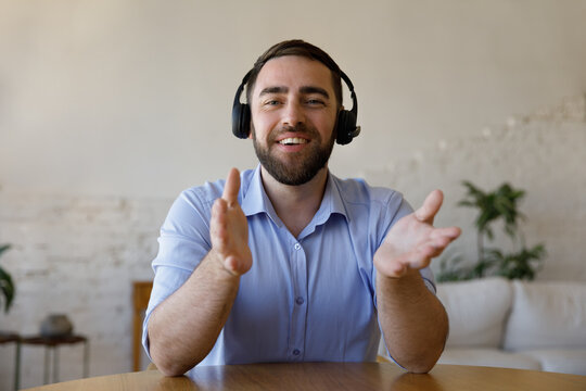 Young man in headphone sit at table looking at cam, makes speech to camera, share knowledge, lead online negotiations, working remotely use videocall app, record new video vlog for subscribers concept