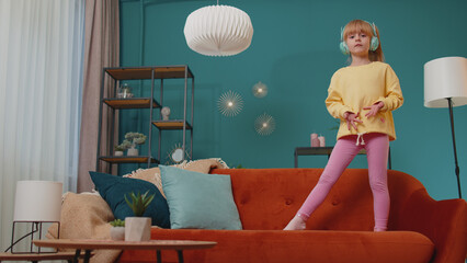 Portrait of Caucasian little happy child girl in headphones dancing and jumping while listening to...