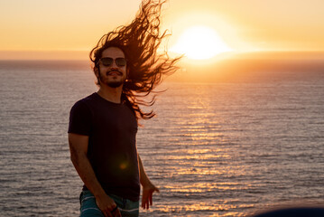 Young man with long black hair at the beach during sunset