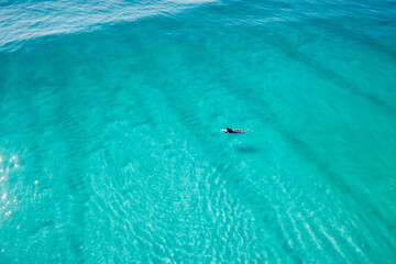 Fototapeta premium Surfer on surfboard in transparent ocean waiting wave. Aerial view
