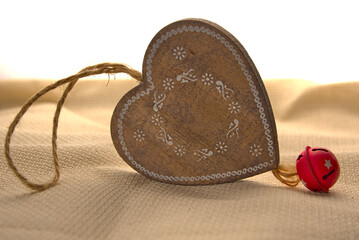 Wooden heart with a red metal bell on a beige linen background.
