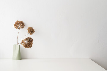 White desk with  minimal vase with a decorative dried branches, flower against white wall.