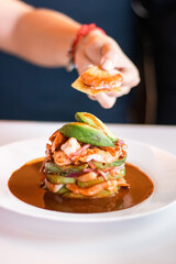 Mano sosteniendo totopo con camar&oacute;n frente a torre de mariscos 