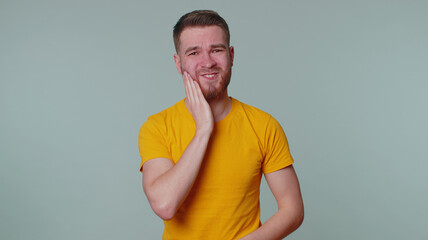Bearded young man touching sore cheek suffering from toothache cavities or gingivitis waiting for...