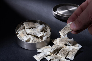 Closeup of metallic Swedish snus can with white portions of smokeless tobacco pouches against a...