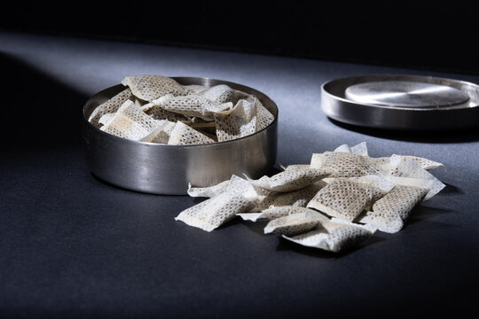 Closeup of metallic Swedish snus can with white portions of smokeless tobacco pouches against a dark background.