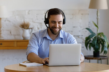 Smiling handsome young man wear headset sit in front of laptop, e-learns, take part in online study...