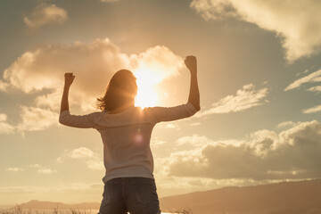 Strong and determined young woman flexing her arms up to the sunset sky. People power, and strength concept 