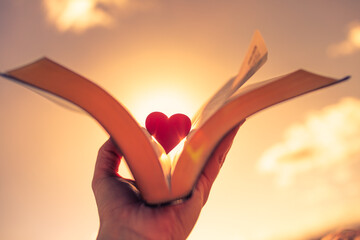 Hand holding book, bible up to the sunlight with silhouette of heart. Faith hope and love concept. Religious belief symbol. 